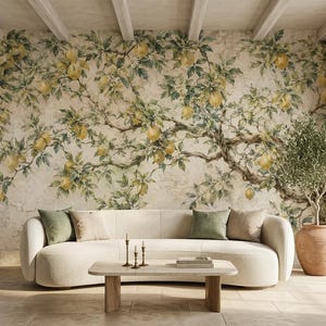 May include: A wall mural featuring a sprawling lemon tree with yellow fruit and green leaves against a textured beige background. A curved cream-colored sofa with green and beige throw pillows sits in front of the mural, with a wooden coffee table.
