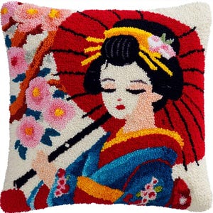 May include: A square throw pillow featuring a textured punch needle design of a figure with black hair, wearing a blue kimono with a yellow obi, holding a large red umbrella, surrounded by pink cherry blossoms against a cream-colored background.