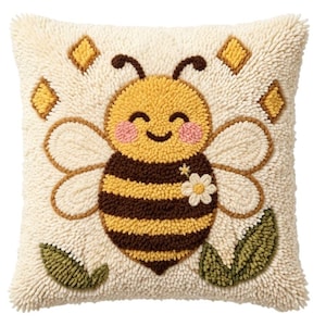 May include: A square throw pillow featuring a textured punch needle design of a smiling bee with yellow and brown stripes, pink cheeks, and white wings. The bee is accented by a small white flower, green leaves, and yellow diamond shapes on a cream background.