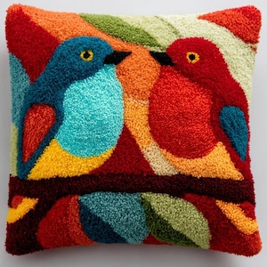 May include: A square throw pillow featuring a textured punch needle design of two birds facing each other on a branch. The birds are rendered in vibrant shades of blue, red, yellow, and orange, set against a background of green and red foliage.