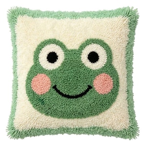 May include: A square throw pillow featuring a tufted, textured surface with a central frog face design. The frog is green with large white eyes, black pupils, pink circular cheeks, and a black curved mouth, set against a cream background.