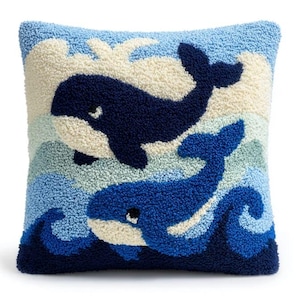 Op de afbeelding: Een vierkant sierkussen met een getextureerd punch needle ontwerp van twee walvissen die in oceaangolven zwemmen. De bovenste walvis is donker marineblauw en de onderste is lichtblauw, beide met crèmekleurige buiken tegen een blauwe achtergrond.