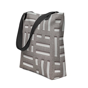 Peut inclure: Un sac fourre-tout présentant un fond texturé brun clair et gris avec un motif répétitif de barres rectangulaires blanches disposées en grille. Le sac comprend deux bandoulières en tissu noir fixées sur le bord supérieur.