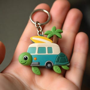 Könnte beinhalten: Ein Schlüsselanhänger in Form einer grünen Schildkröte, die wie ein blaugrüner und cremefarbener Campingbus gestaltet ist. Die Schildkröte hat eine braune Palme und ein gelbes Surfbrett auf dem Dach. Ein silberner Metallring dient zur Befestigung.