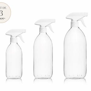 Op de afbeelding: Drie doorzichtige glazen spuitflessen van verschillende groottes met witte plastic sproeikoppen. Een cirkelvormige afbeelding in de linkerbovenhoek bevat de tekst LOT DE 3 en een kleine illustratie van een blaadje.