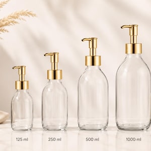 Op de afbeelding: Vier doorzichtige glazen zeepdispensers met goudkleurige pompmechanismen, gerangschikt in oplopende grootte. De flessen zijn gelabeld met een inhoud van 125 ml, 250 ml, 500 ml en 1000 ml, met een consistent ontwerp en een ronde basis.