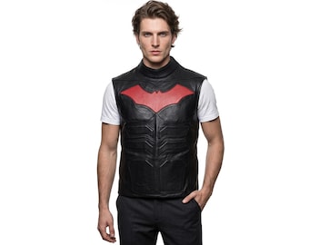 May include: A black leather vest featuring a high mock neck collar and a prominent red bat-shaped emblem on the chest. The vest has molded, segmented paneling across the torso, creating a structured appearance over a plain white short-sleeved t-shirt.