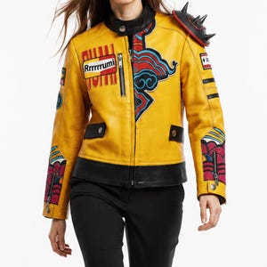 May include: A yellow jacket with black leather trim, a stand-up collar, and a spiked shoulder pad. The jacket features colorful embroidered patches, including one with the text Rrrrrrumi, and decorative patterns on the sleeves and chest.