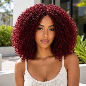 May include: A shoulder-length wig featuring deep burgundy red hair with a tight, coiled, and voluminous texture. The hair is styled with a center part, creating a full, rounded shape that frames the face with dense, springy curls throughout.
