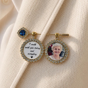 Könnte beinhalten: Eine goldfarbene Brosche im Sicherheitsnadel-Design mit einem blauen Kristallakzent, einem runden Anhänger mit dem Text I walk with you today and everyday und einem kleinen Herz sowie einem runden Anhänger mit einem Foto einer älteren Person.