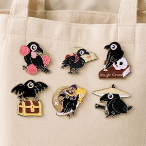 Könnte beinhalten: Ein Set aus sechs schwarzen Raben-Emaille-Pins. Die Motive zeigen einen Raben mit rosa Rosen, einen Raben mit Brief, einen Raben auf einem Buch mit der Aufschrift Magic Crow und Totenkopf, eine Schatztruhe, einen Zauberhut mit Mond und einen Hut.
