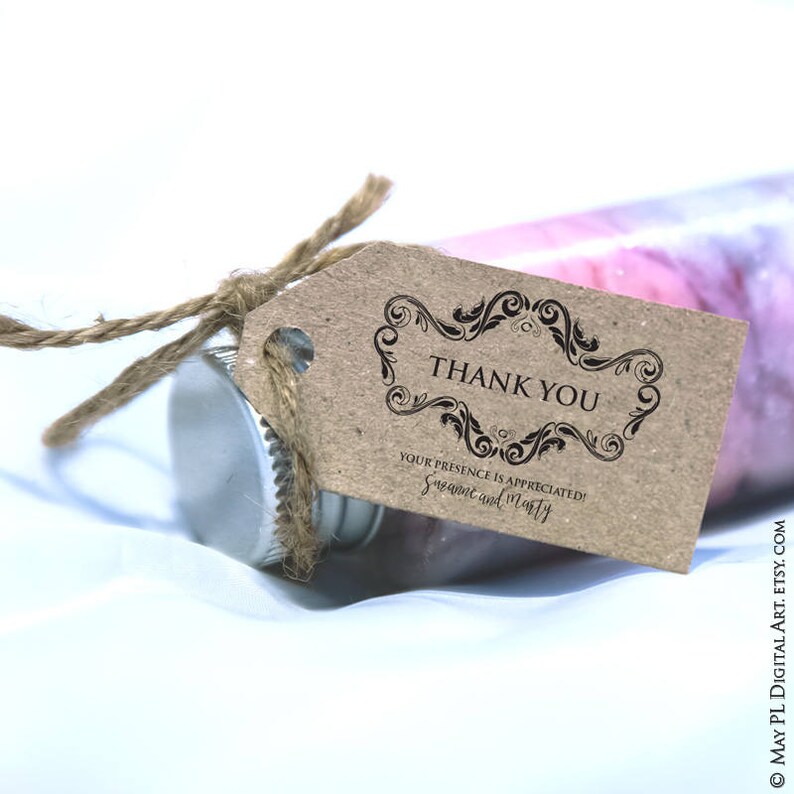 May include: A clear glass bottle with a silver cap and a brown tag tied with twine. The tag reads "THANK YOU" in a decorative frame, with the text "YOUR PRESENCE IS APPRECIATED! Suzanne and Marty" below.
