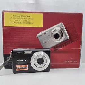 Puede incluir: Una cámara digital negra Casio Exilim EX-Z75 con sensor de 7,2 megapíxeles y lente de zoom óptico 3x, colocada frente a su caja de embalaje original roja y blanca que muestra el modelo de la cámara y las especificaciones técnicas.
