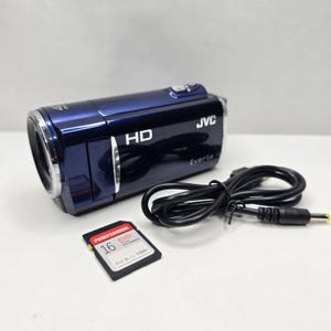 Op de afbeelding: Een donkerblauwe JVC Everio HD camcorder met een zilverkleurige lensrand, vergezeld van een zwarte stroomkabel en een 16GB EVO Plus geheugenkaart. De behuizing bevat de tekst HD, JVC en Everio, en op de geheugenkaart staat Proefssional 16.