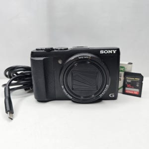 Peut inclure: Un appareil photo numérique Sony noir avec un objectif Sony Lens G, un zoom optique 30x et des spécifications 3,5-6,3/4,3-129. Sont inclus un câble de charge USB noir, une batterie NP-BX1 blanche et une carte mémoire SanDisk 16 Go.