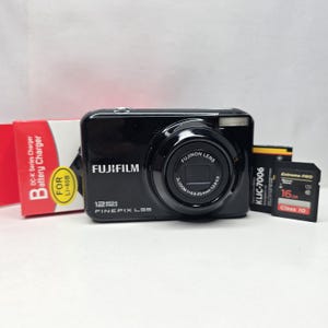 Op de afbeelding: Een zwarte Fujifilm FinePix L55 digitale camera met 12 megapixels en een Fujinon-lens. Inbegrepen zijn een rood-witte DC-K Series batterijladerdoos voor LI-40B, een KLIC-7006 batterij en een 16GB Extreme Pro SD-geheugenkaart.
