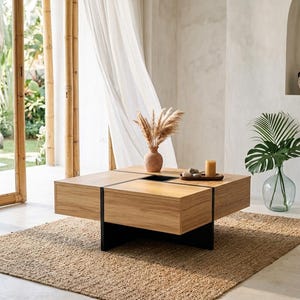 May include: A square coffee table constructed from light-toned wood with a smooth finish, featuring a black metal base and a central square cutout. The table surface holds a small terracotta vase with dried pampas grass and a candle.