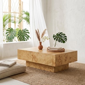 May include: A rectangular coffee table crafted from light-toned burl wood with a prominent grain pattern. The table features a thick, solid top supported by a recessed base of the same material, creating a floating effect. The surface is smooth and flat.