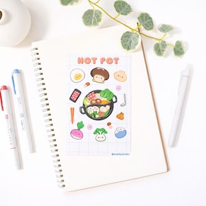 May include: A spiral-bound notebook with a sticker sheet featuring a cartoon hot pot design. The sticker sheet includes illustrations of food items like mushrooms, eggs, and vegetables. Two pens, one red and one blue, are on the left side of the notebook.