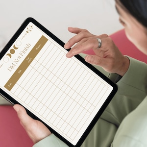 May include: A black tablet displaying a digital planner with the text "Did Not Finish" in a gold color. The planner has a grid layout with columns for date, task, and notes, and is decorated with moon phase and floral elements.