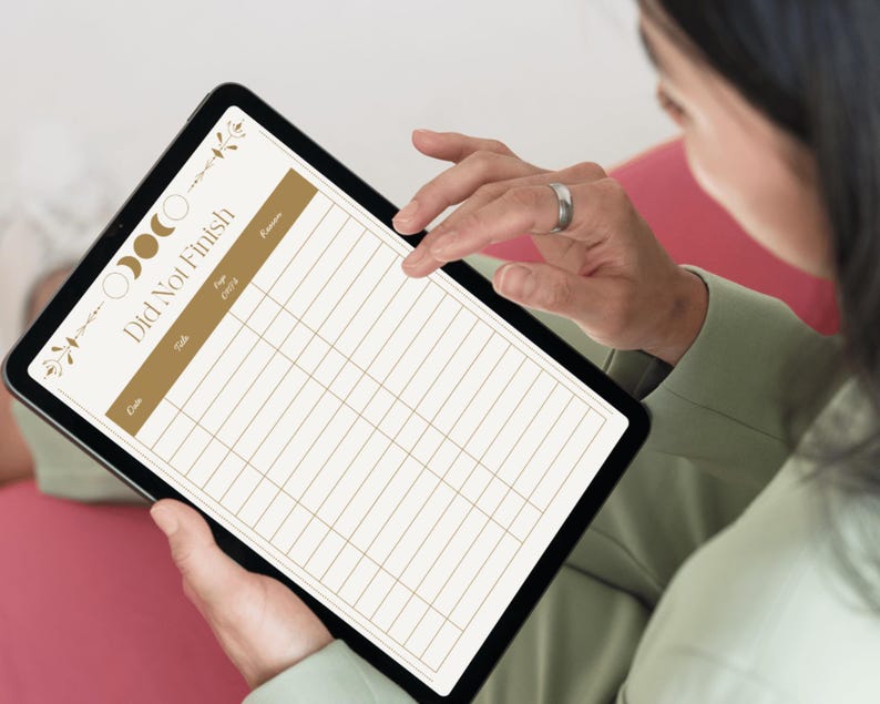 May include: A black tablet displaying a digital planner with the text "Did Not Finish" in a gold color. The planner has a grid layout with columns for date, task, and notes, and is decorated with moon phase and floral elements.
