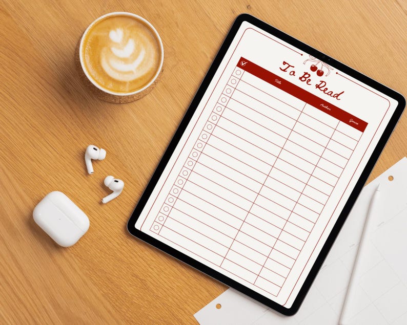 May include: A digital tablet displaying a "To Be Read" list with a cherry design, a cup of coffee with latte art, wireless earbuds, and a charging case on a wooden surface.