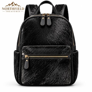 May include: A black backpack with a textured hair-on-hide finish, featuring a main zippered compartment, a front zippered pocket, and two side pockets. The bag includes gold-tone metal zippers with black leather pulls and adjustable shoulder straps.