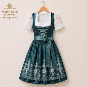 May include: A dark teal dirndl dress featuring a white lace blouse with short sleeves, a square neckline, and a bodice with a lace-up front. The skirt has a floral pattern at the hem and a matching teal satin ribbon tied in a bow at the waist.