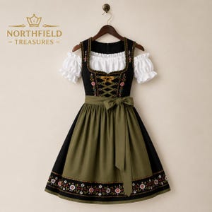 May include: A black dirndl dress featuring a white off-the-shoulder blouse with ruffled sleeves, an olive green apron with a bow, and floral embroidery on the bodice and hem. The Northfield Treasures logo is visible in the top left corner.