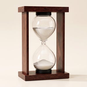 Puede incluir: Un reloj de arena con un marco de madera de color marrón oscuro con soportes verticales y bases horizontales superior e inferior. El bulbo de vidrio central contiene arena blanca, con parte de la arena descansando en la cámara inferior.