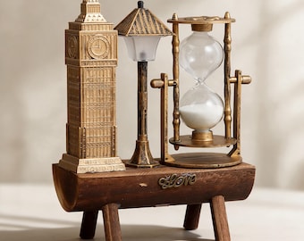 Può includere: Un ornamento decorativo da tavolo con una replica dorata del Big Ben, un lampione e una clessidra rotante con sabbia bianca, il tutto montato su una base in legno marrone scuro con la parola Love in caratteri metallici sul davanti.