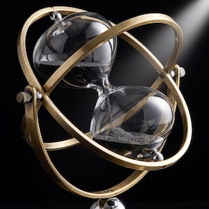 Pu&ograve; includere: Una clessidra con bulbi in vetro trasparente contenenti sabbia nera fine, racchiusa in una cornice metallica rotante color ottone composta da due anelli intersecanti. La struttura presenta piccole manopole metalliche sui lati per la rotazione.