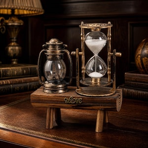 May include: A decorative wooden stand with four legs features a metal lantern containing a miniature Eiffel Tower and a rotating hourglass filled with white sand. The word Love is attached to the front of the wooden base in metal script lettering.