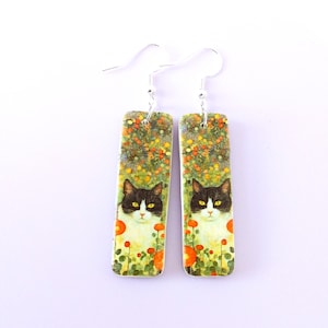 Zwart-witte kat met bloemen oorbellen gemaakt van polymeerklei, illustratie katten sieraden oorbellen