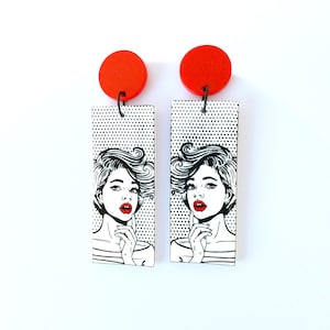 Könnte beinhalten: Ein Paar rote und weiße Ohrringe mit einem Pop-Art-Design, das ein Frauen Gesicht zeigt. Die Ohrringe sind aus Holz und haben ein schwarz-weißes Punkte-Muster.