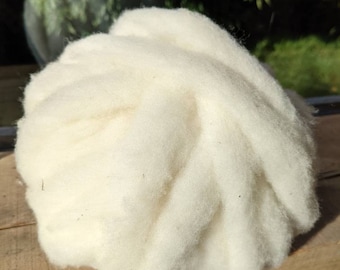 May include: A large, fluffy ball of undyed, off-white wool fibers. The wool appears soft and cloud-like, with a slightly textured surface. The fibers are tightly packed together, suggesting a high-quality material for crafting or textile projects.