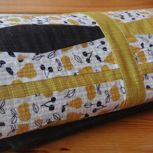 Pode incluir: Edredão enrolado com um design de patchwork em amarelo, preto e branco. O edredão apresenta um padrão repetido de peras e cerejas. O edredão é feito de tecido macio e é adequado para uma cama ou um sofá.