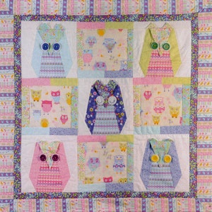 Puede incluir: Un edredón hecho a mano con nueve diseños de búhos. Cada búho está hecho con diferentes telas estampadas y ojos de botón. El edredón tiene un fondo blanco con un borde colorido, ideal para una habitación infantil.