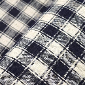 Puede incluir: Una tela tejida que presenta un patrón de cuadros en contraste de color negro y blanco roto. El textil muestra una estructura de rejilla visible con cuadrados oscuros y claros alternos, creando un diseño geométrico repetitivo en toda la superficie.