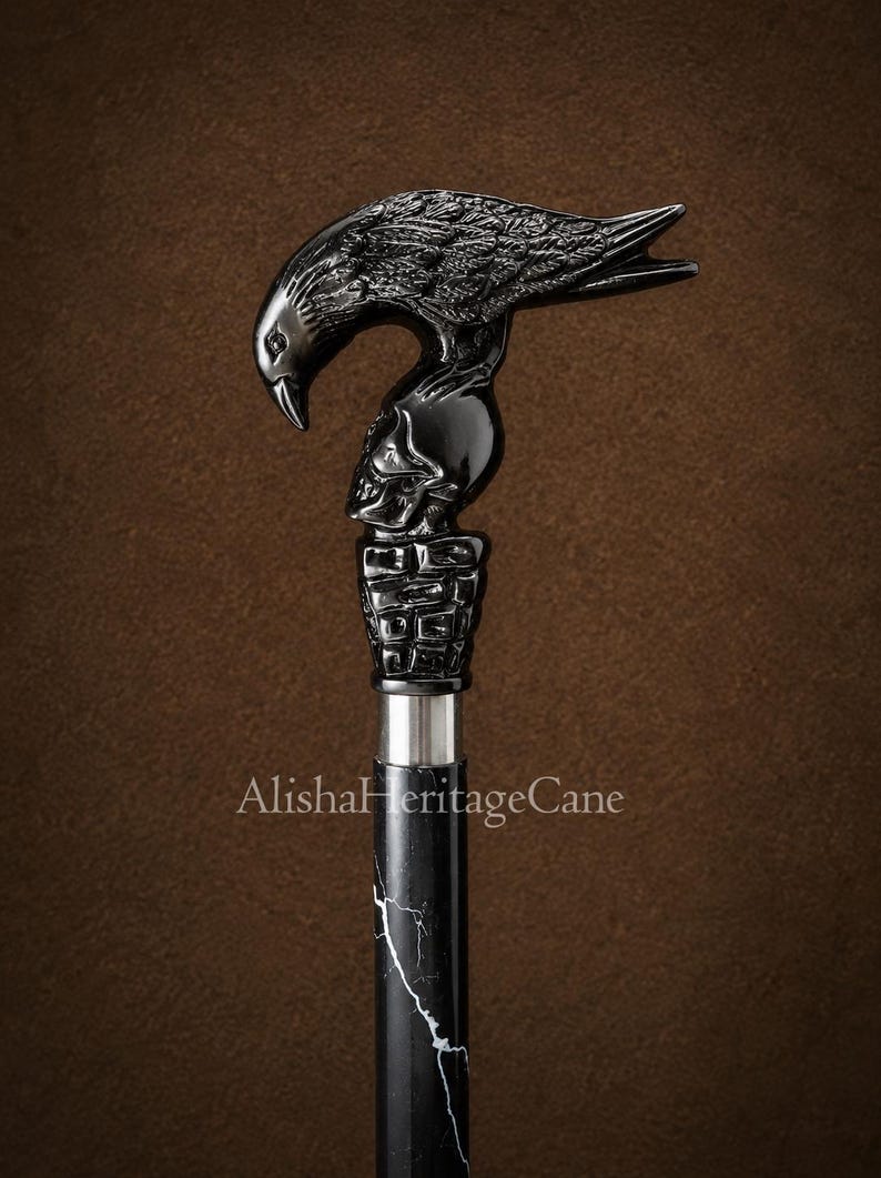 May include: A walking cane featuring a black handle shaped like a raven perched atop a human skull, which rests on a textured base. The shaft is black with white marble-like veining. The text AlishaHeritageCane is printed on the shaft.