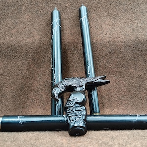 May include: A black walking stick handle featuring a carved raven perched atop a skull. The handle is attached to a black shaft with white marble-like veining. Two additional matching shaft segments are positioned vertically behind the handle.