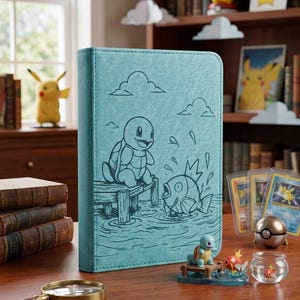 Op de afbeelding: Een blauwgroene verzamelkaartenmap met een lijntekening van een Squirtle op een houten steiger en een Magikarp die in het water spat. De kaft bevat eenvoudige wolkenomtrekken en heeft een gestructureerde afwerking op de voorzijde.