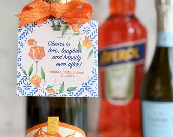 Puede incluir: Etiqueta de regalo de ducha nupcial naranja y azul con el texto "Cheers to love, laughter and happily ever after! Moira's Bridal Shower 05.17.2025". La etiqueta está atada a una pequeña botella de vino espumoso con sabor a naranja con una tapa dorada.