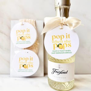 May include: A mini Freixenet Prosecco bottle with a cream-colored ribbon and a round white tag featuring a yellow lemon graphic and the text "pop it when she pops" and "ENJOY A TOAST WHEN BABY BARSOOM ARRIVES," alongside two matching circular tags.