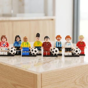 Könnte beinhalten: Eine Sammlung von Lego-Fußballspielerfiguren, die jeweils einen Fußball halten. Die Spieler tragen verschiedene Trikots, darunter rot, gelb, blau und weiß. Jede Figur hat eine einzigartige Frisur und einen Gesichtsausdruck.