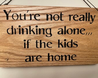 Wooden sign saying you’re not really drinking alone if the kids are home. Funny sign. Drinking sign.