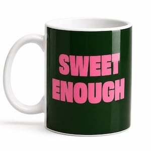 May include: A dark green ceramic mug with a white interior and handle. The exterior features the text SWEET ENOUGH printed in bold, capital pink letters centred on the front. The mug has a cylindrical shape with a smooth, glossy finish.