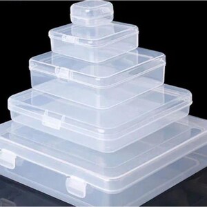 May include: A stack of four clear, rectangular plastic storage boxes with hinged lids and snap closures. The boxes are arranged in descending order of size, with the smallest container at the top and the largest container at the base.