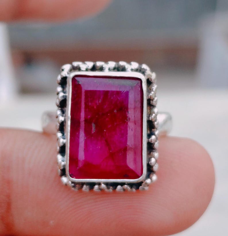 May include: A silver ring featuring a large, rectangular, deep pink gemstone with visible internal fractures. The stone is set within a textured, beaded silver frame that surrounds the entire perimeter of the rectangular setting.