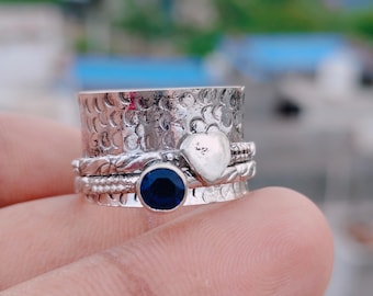 Anel giratório em prata de lei com safira azul, anel de meditação com aro largo martelado e detalhe de coração.